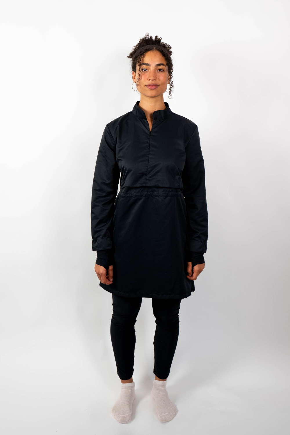 Frontalansicht einer Frau, die eine schwarze Sport-Tunika mit Stehkragen, Taillenzug und geschichtetem Look trägt.