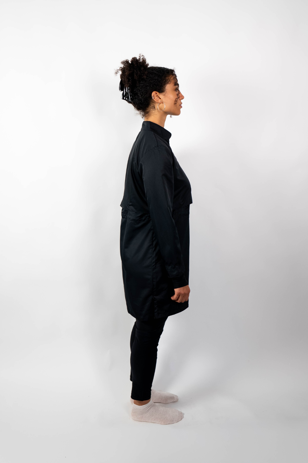 Seitenansicht einer Frau, die eine schwarze Sport-Tunika mit Stehkragen und einem geschichteten Look durch einen Taillenzug trägt.
