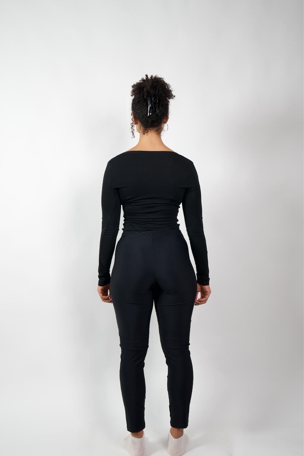 Rückenansicht einer Frau in schwarzen, eng anliegenden Leggings und einem schwarzen Langarmshirt.