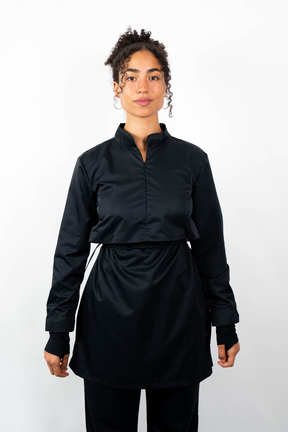 Frontalansicht einer Frau, die eine schwarze Sport-Tunika mit Stehkragen, Taillenzug und geschichtetem Look trägt.
