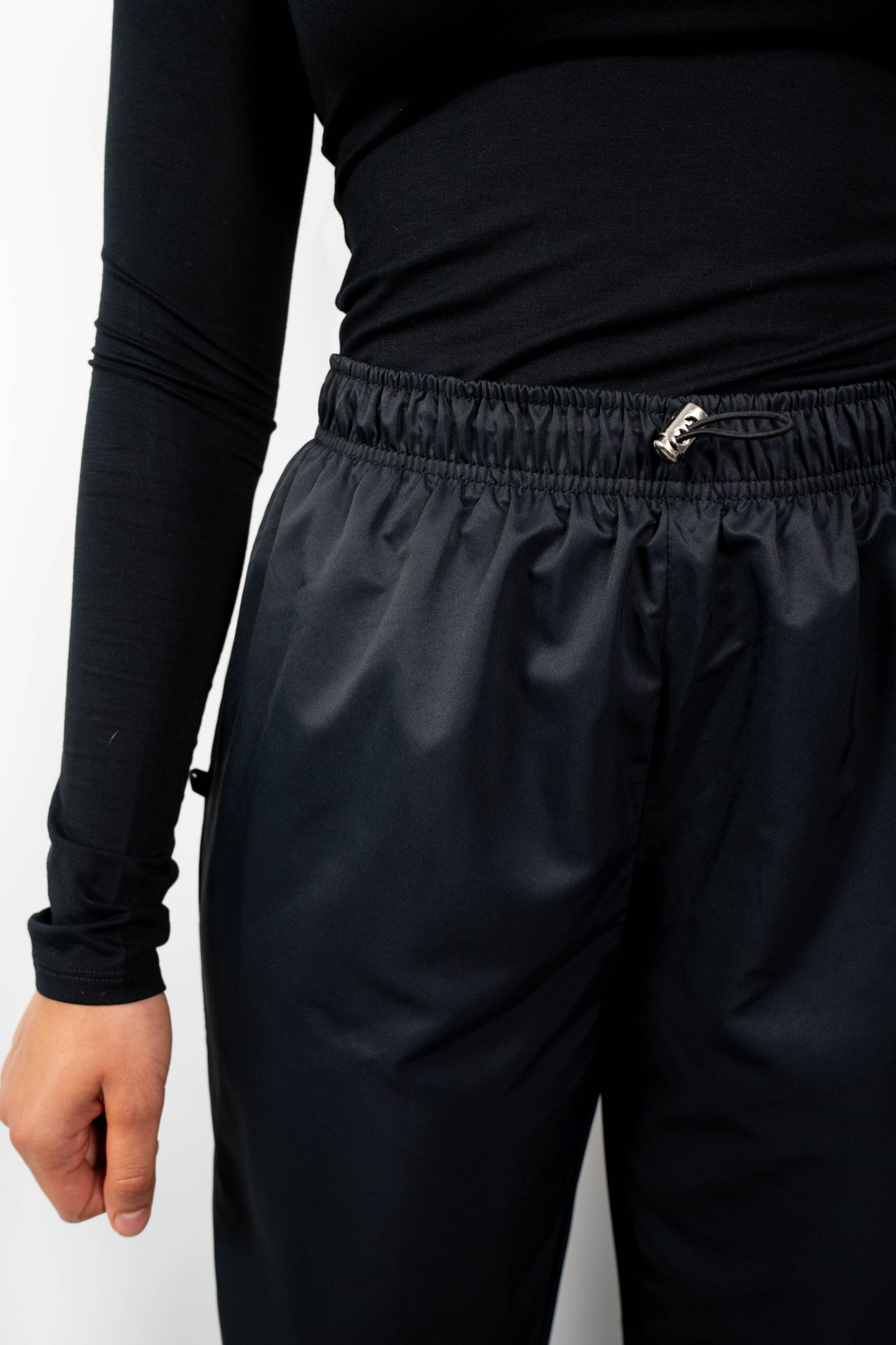 Nahaufnahme des Bundes der schwarzen, lockeren Badehose, die den elastischen, gerafften Bund und den Taillenzug mit silberner Kordelbremse zeigt.