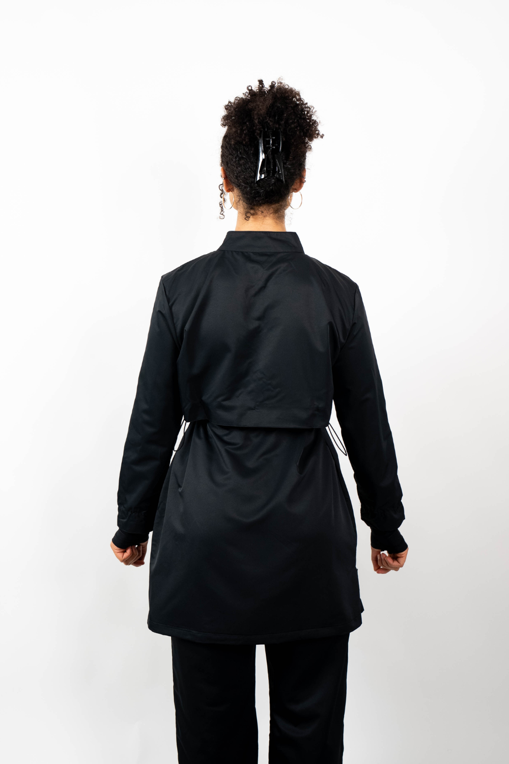 Rückenansicht einer Frau, die eine schwarze Sport-Tunika mit Stehkragen und einem geschichteten Look durch einen Taillenzug trägt.