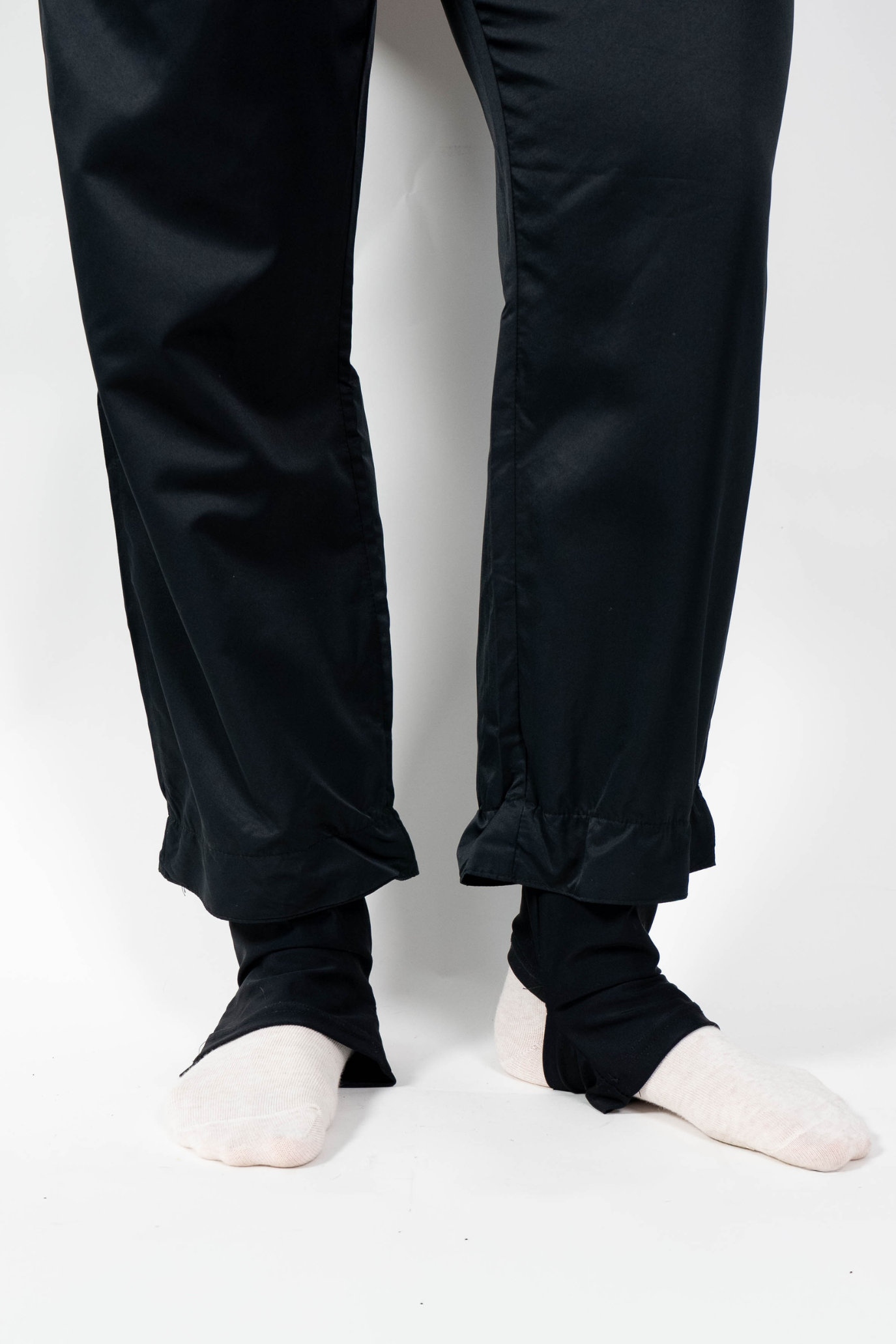 Nahaufnahme des Beinabschlusses der schwarzen, weiten Badehose. Der Saum ist durch einen Gummizug gerafft und zeigt die schwarzen Bündchen mit Fußschlaufe an den Knöcheln.