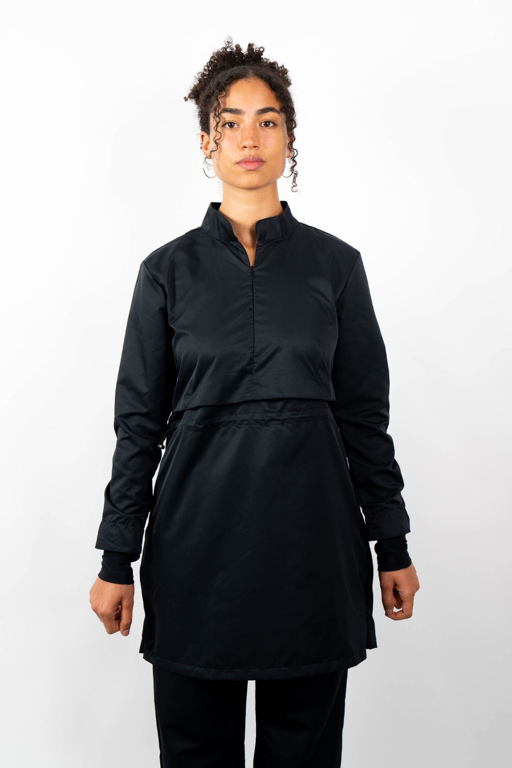 Frontalansicht einer Frau, die eine schwarze Sport-Tunika mit Stehkragen, Taillenzug und geschichtetem Look trägt.