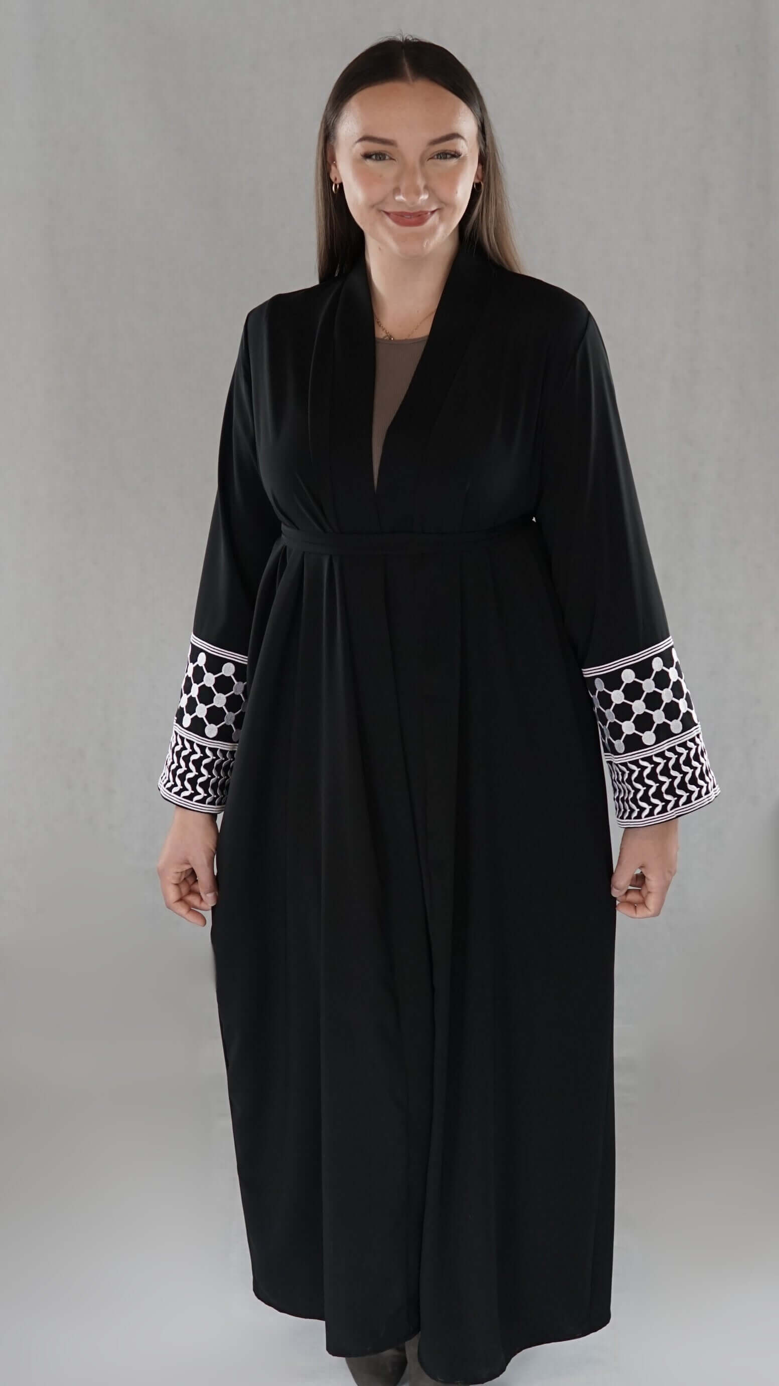 Schwarze Abaya mit traditionellen palästinensischen Mustern an den Ärmeln, präsentiert von einer jungen Frau.