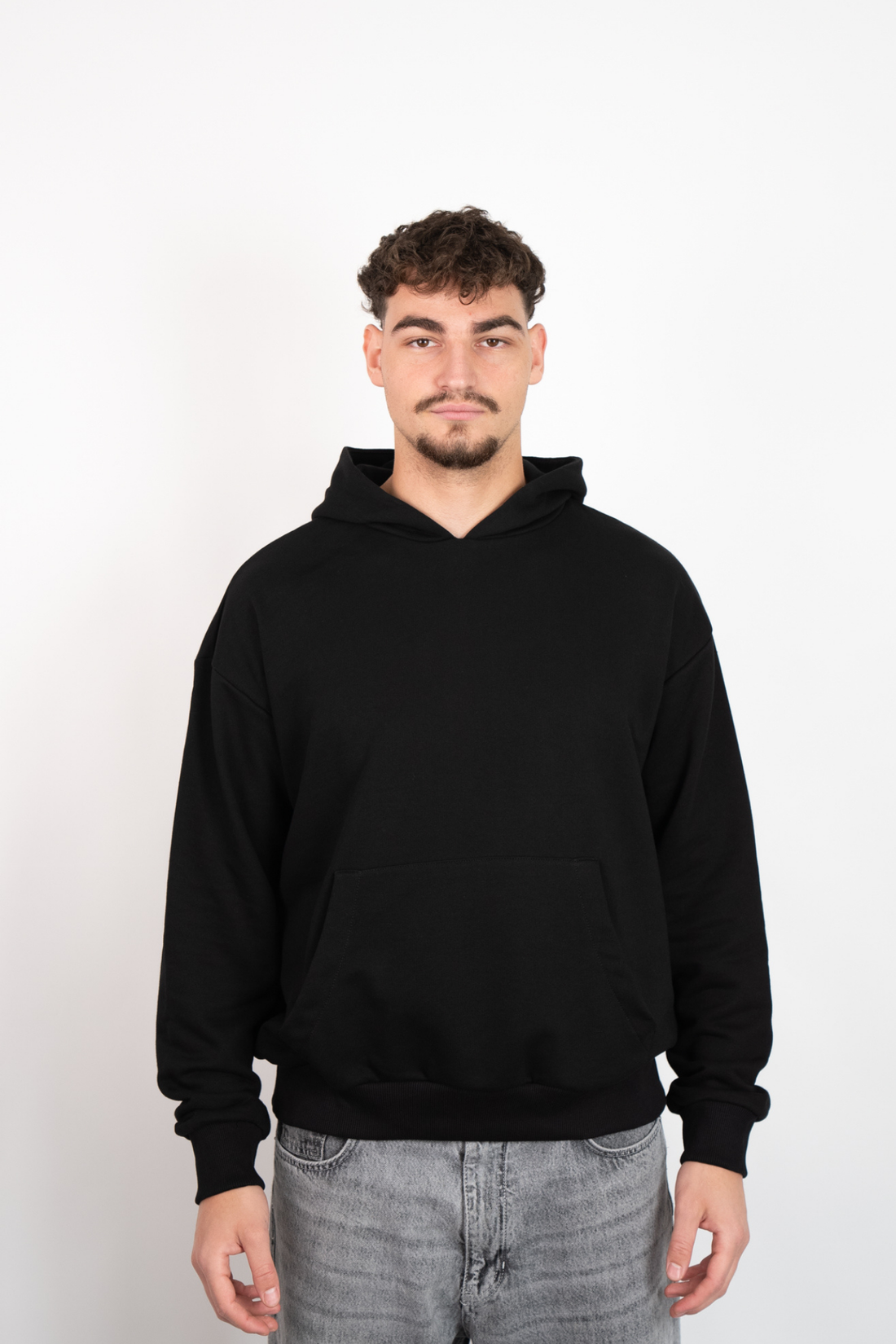 Schwarzer Oversize Hoodie mit Kapuze und Kängurutasche, getragen von einem Mann in grauen Jeans.