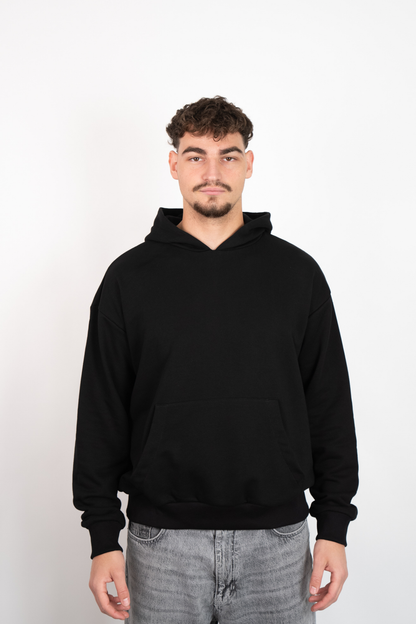Schwarzer Oversize Hoodie mit Kapuze und Kängurutasche, getragen von einem Mann in grauen Jeans.