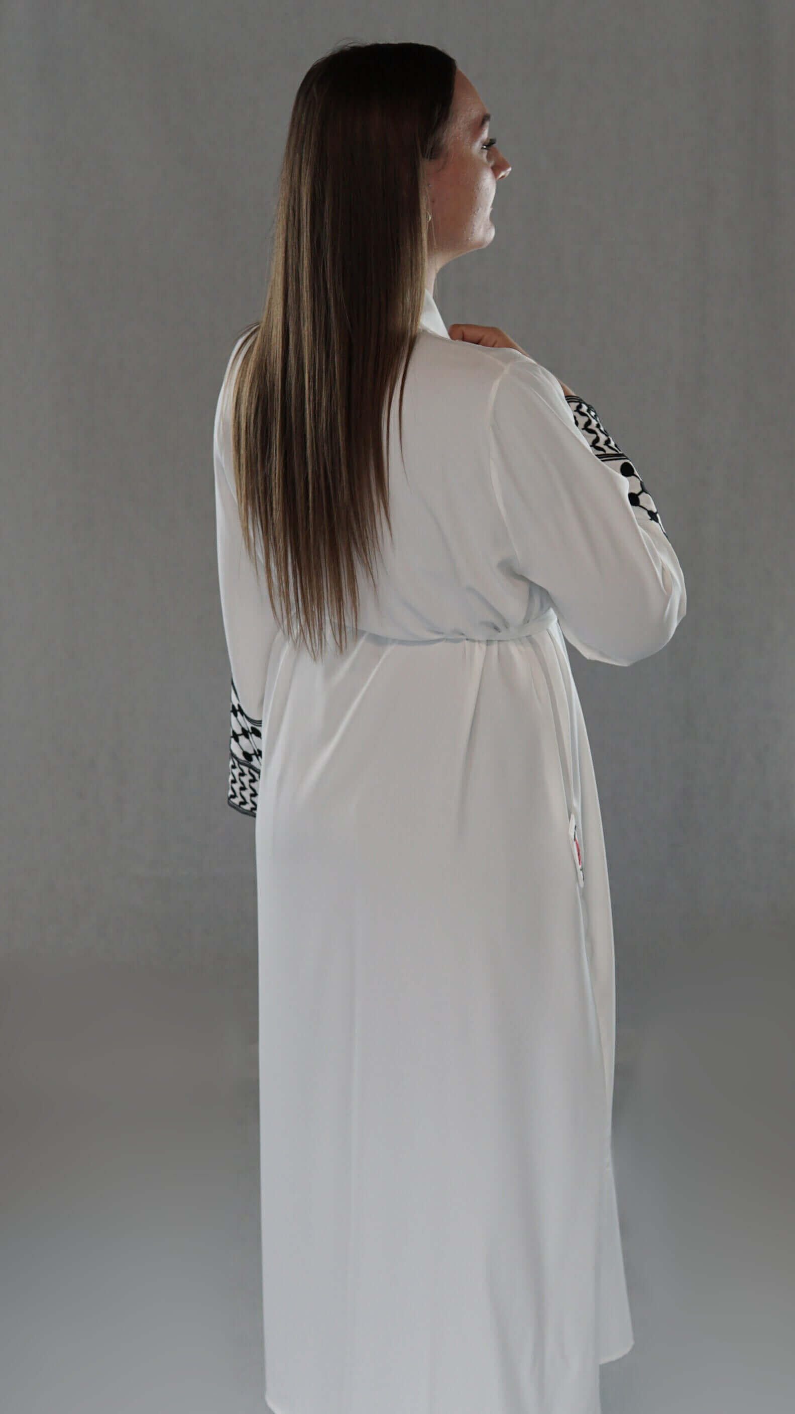 Woman in a white abaya with traditional Palestinian designs, showcasing cultural elegance and modern style.