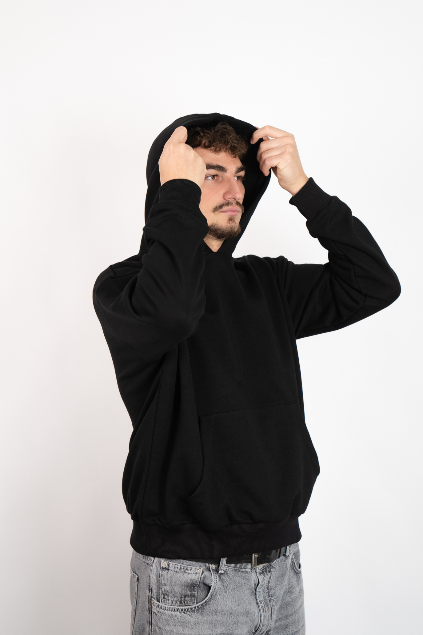 Nahaufnahme eines Mannes, der einen schwarzen Oversize Hoodie trägt und sich die Kapuze aufsetzt oder anpasst.