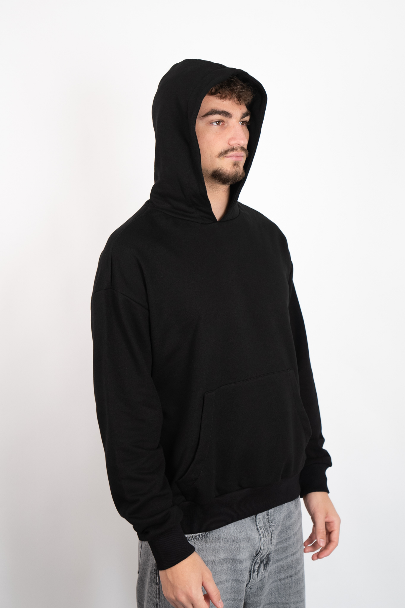 Seitenansicht eines Mannes in einem schwarzen Oversize Hoodie mit aufgesetzter Kapuze.