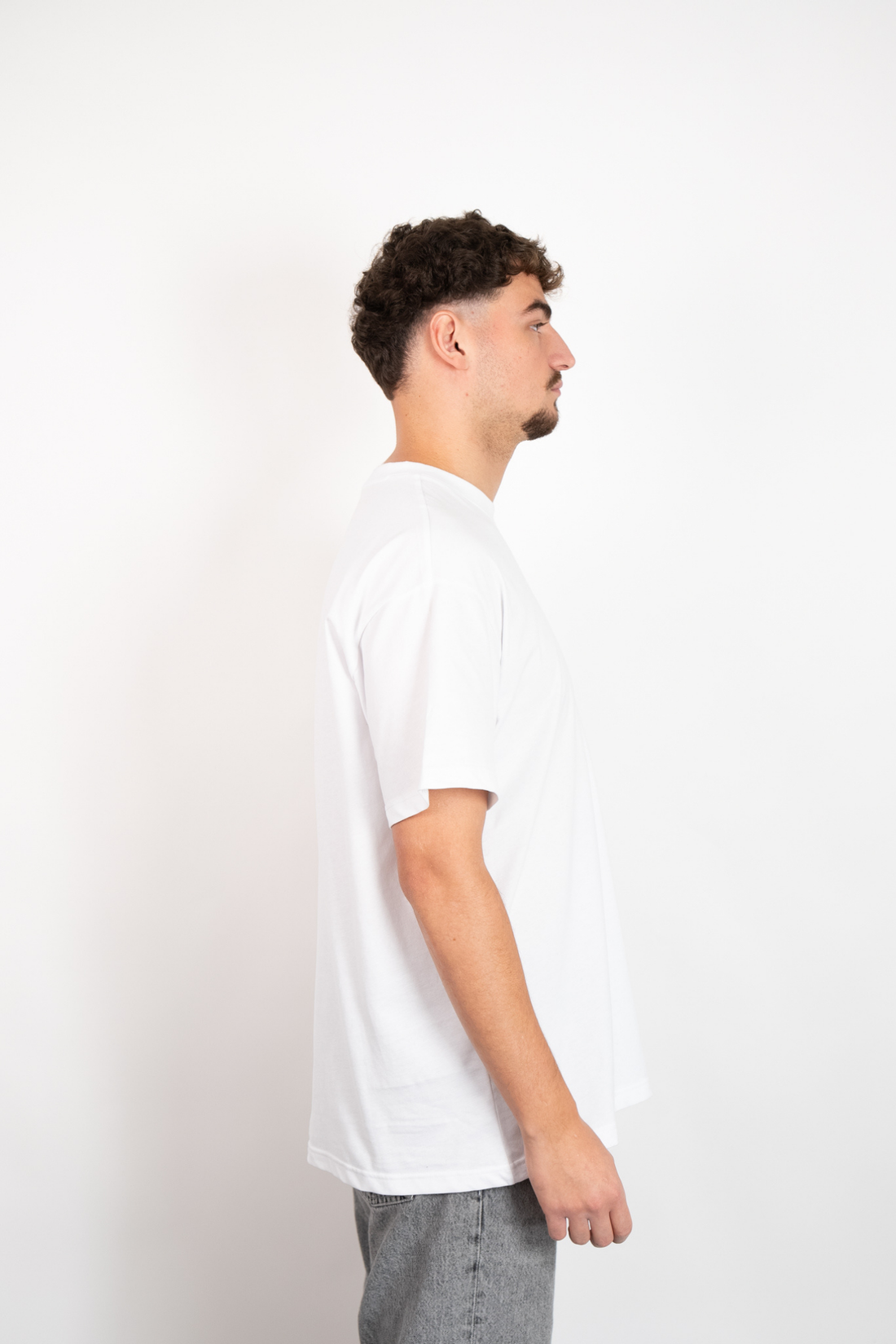 Weißes Oversize T-Shirt aus 100% Baumwolle mit Rundhalsausschnitt, getragen von einem Mann in Seitenansicht.