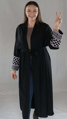 Schwarze Abaya mit palästinensischem Design, elegant und traditionell, präsentiert von Model mit friedlichem Zeichen.