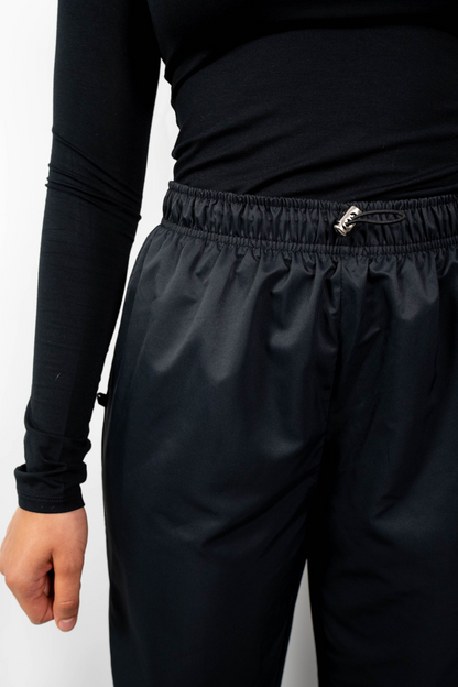Nahaufnahme des Bundes der schwarzen, lockeren Badehose, die den elastischen, gerafften Bund und den Taillenzug mit silberner Kordelbremse zeigt.