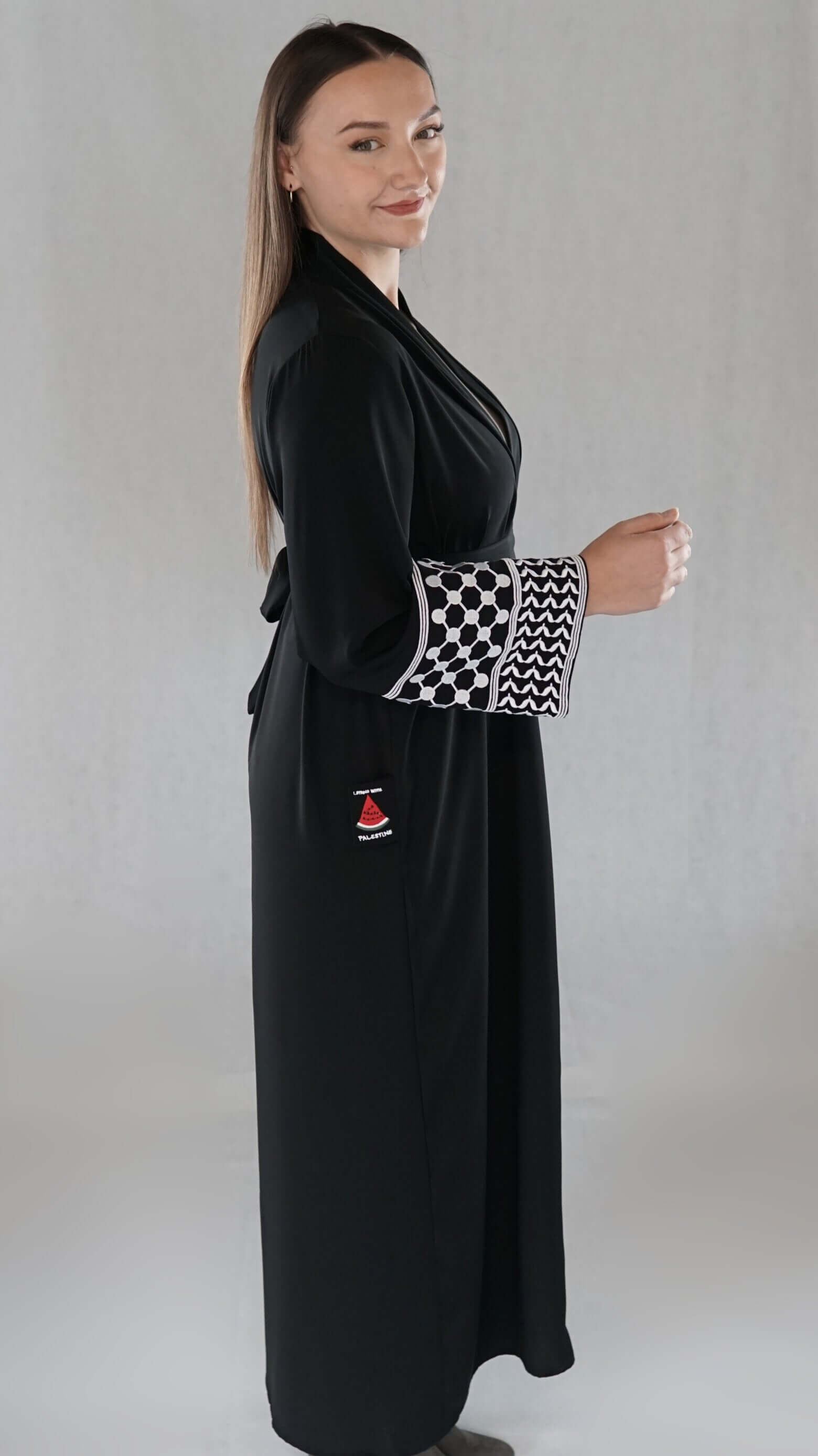 Schwarze Abaya mit palästinensischem Design und elegantem Muster auf den Ärmeln, präsentiert von einer Frau.