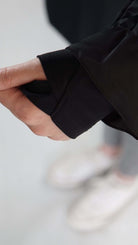 Close-up of a hand adjusting the sleeve of a black garment, showcasing detailed stitching and fabric texture.