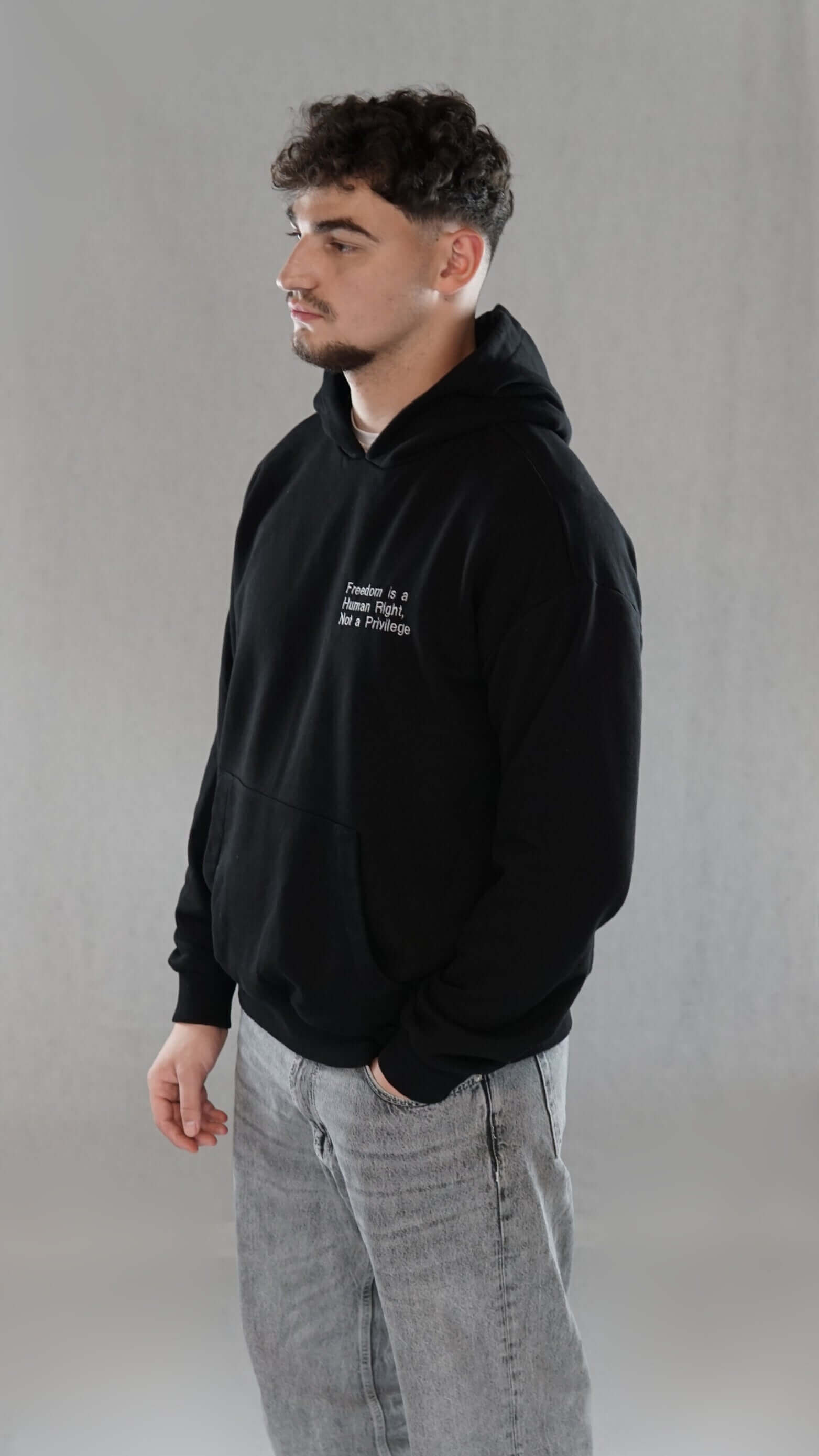 Man wearing an oversize black hoodie with the slogan "Freedom is a human right, not a privilege" on the chest, promoting comfort and style.