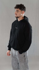 Man wearing black oversize hoodie with minimalist "Mu 'min" embroidery, showcasing modern and spiritual style.