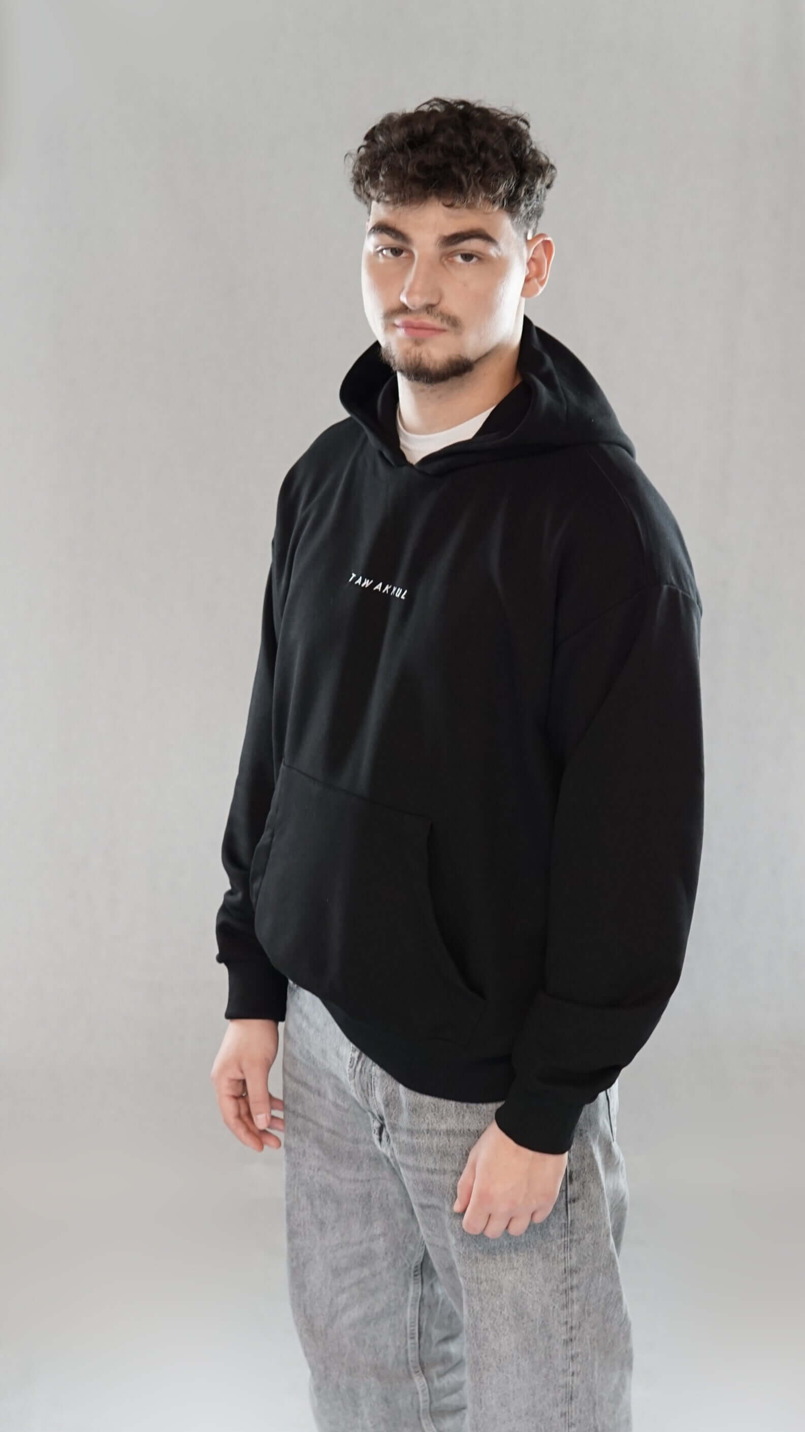 Man wearing black oversize hoodie with "Tawakkul" text on front, showcasing faith-inspired design and comfortable fit.