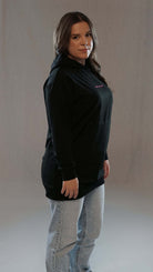 Woman wearing a black Muminah Damen Hoodie, showcasing long fit and comfortable style paired with jeans.