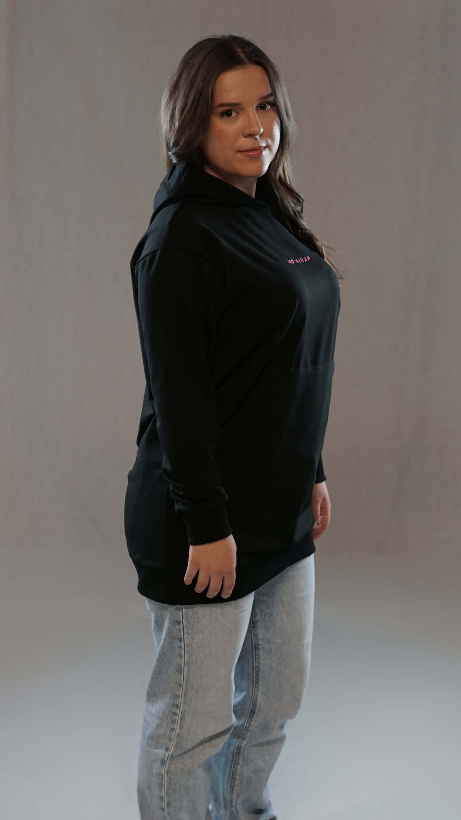 Woman wearing a black Muminah Damen Hoodie, showcasing long fit and comfortable style paired with jeans.