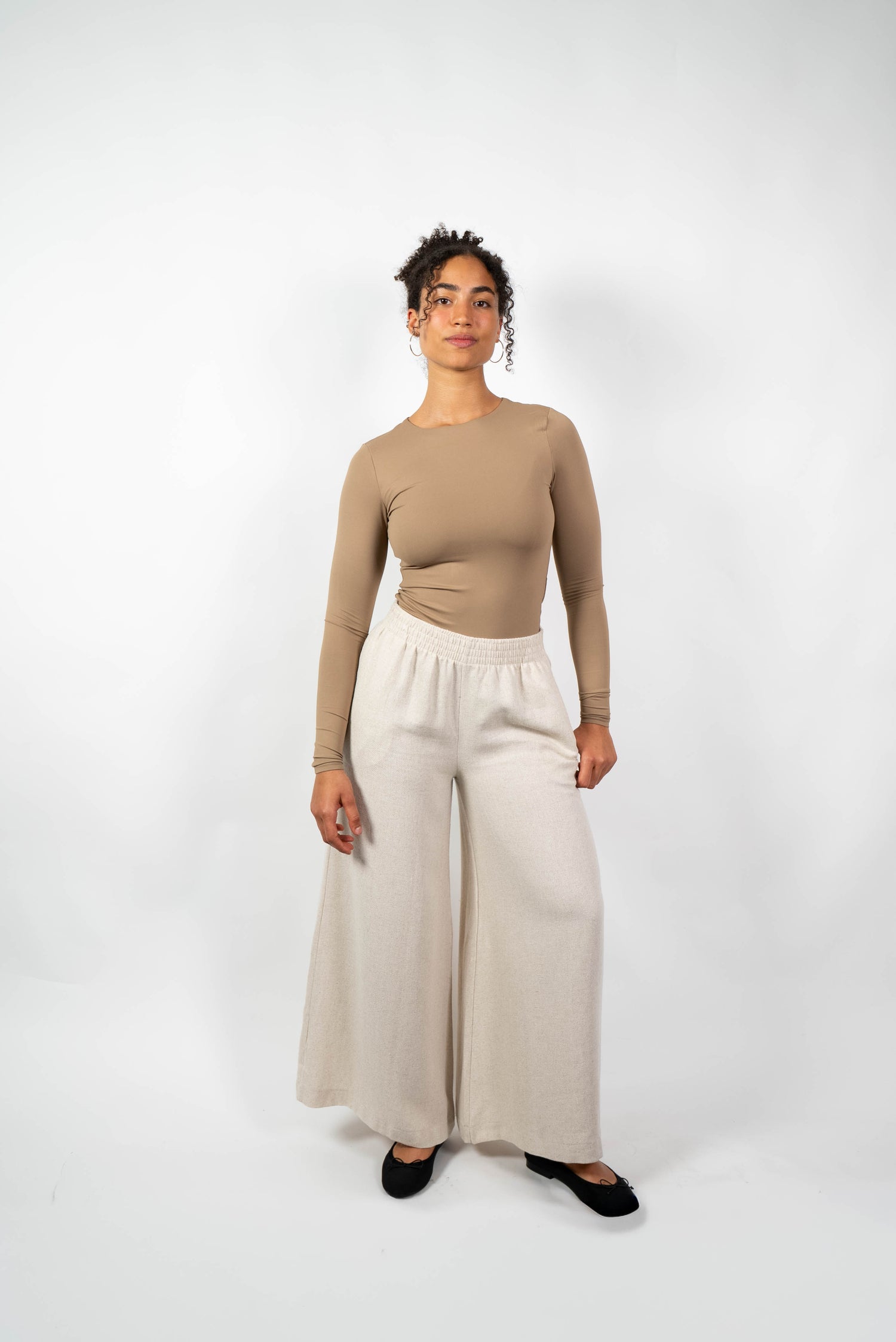 Weite, cremefarbene (oder hellbeige) Hose im Culotte- oder Marlene-Stil aus weichem Material mit elastischem Bund, getragen von einer Frau.