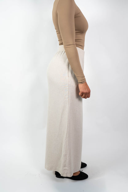 Seitenansicht einer Frau in einer cremefarbenen, weiten Marlene-Hose mit hohem, elastischem Bund und einem eng anliegenden, beige/braunen Oberteil.