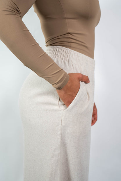 Nahaufnahme der cremefarbenen, weiten Marlene-Hose von der Seite, die die seitliche Eingrifftasche und den elastischen Bund zeigt.