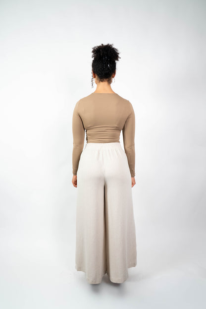 Rückenansicht einer Frau in einer cremefarbenen, weiten Marlene-Hose mit elastischem, gerafftem Bund und einem eng anliegenden, beige/braunen Oberteil.