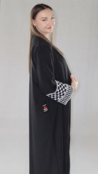 Schwarze Abaya mit palästinensischem Design, präsentiert von einer Frau mit elegantem Auftreten.